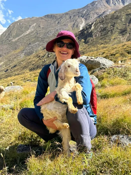 Lenka smiling with a young goat in her arms in a Himalayan valley