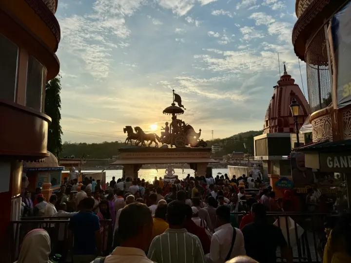 Crowd gathering for the evening Ganga Aarti in Rishikesh at sunset, with the chariot sculpture of Krishna and Arjuna above the gate