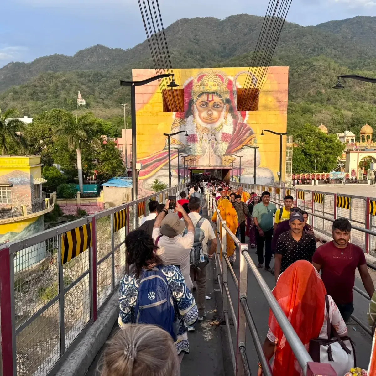 Pilgrims crossing the suspension bridge in Rishikesh towards a large mural of Hanuman