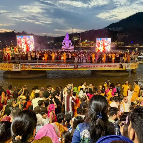 Evening Ganga Aarti on the Ganges in Rishikesh, with a seated Shiva statue and priests holding lamps on the ghat