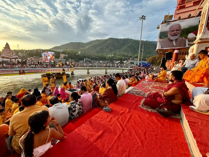 Devotees seated on the ghat in Rishikesh during the evening Ganga Aarti, the river and hills behind