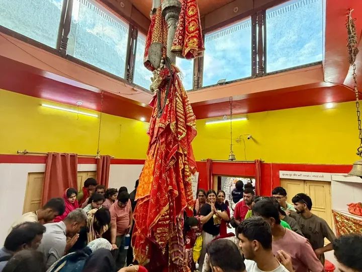 The giant trident of the Shakti Temple in Uttarkashi, wrapped in red cloth, with devotees praying below