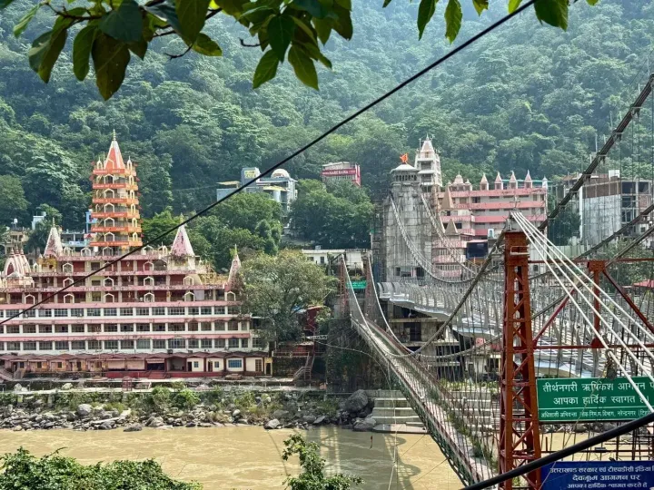 The tiered Trayambakeshwar temple and the Lakshman Jhula suspension bridge over the Ganges in Rishikesh, forested hills behind