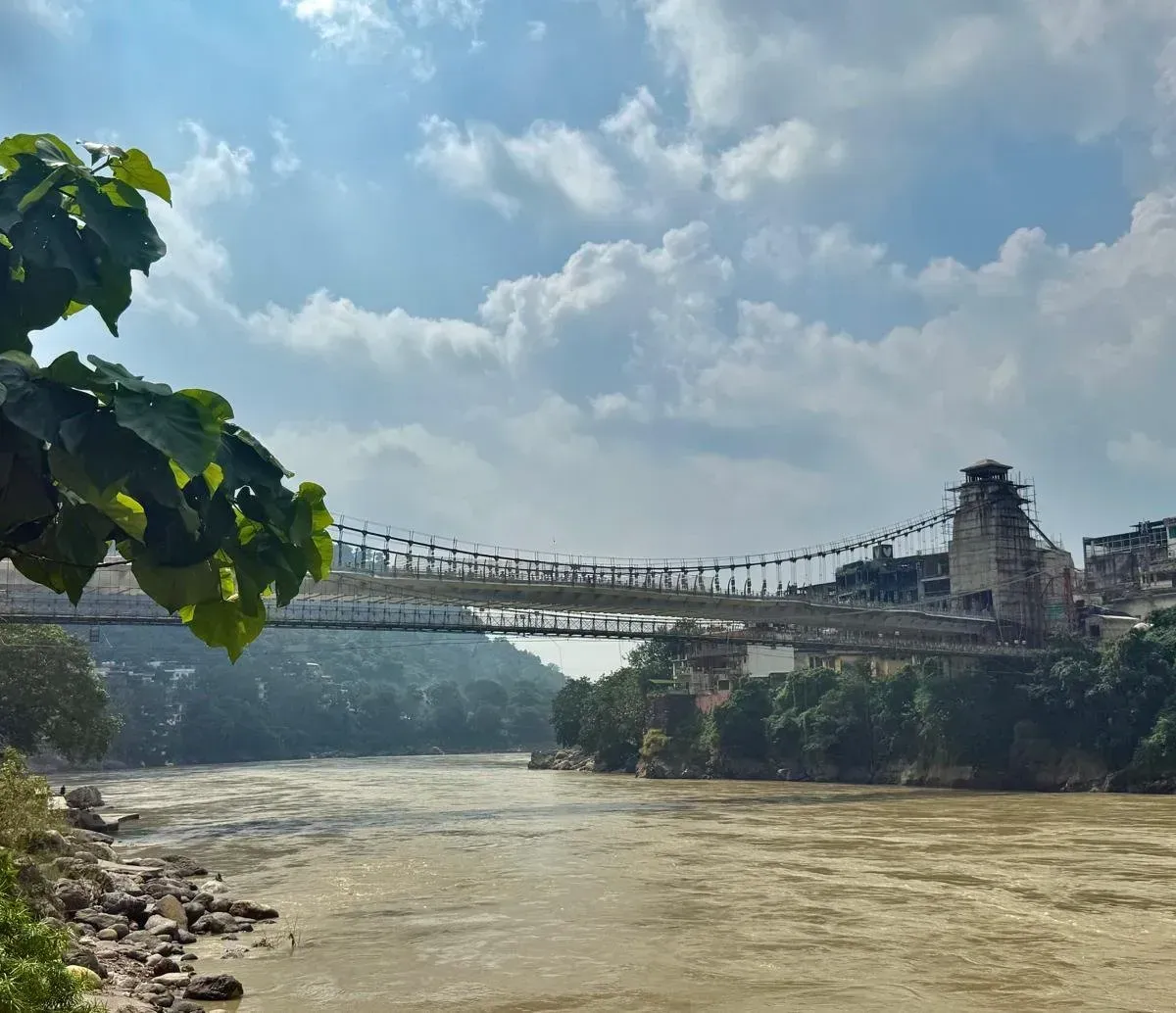 Suspension bridge across the wide, monsoon-brown Ganges in Rishikesh under a cloudy sky