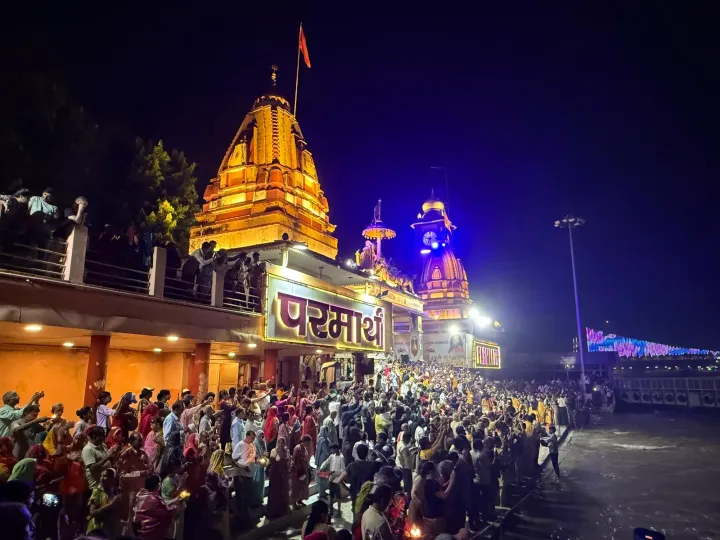 Parmarth Niketan ashram lit up at night during the Ganga Aarti, with crowds on the ghat by the river