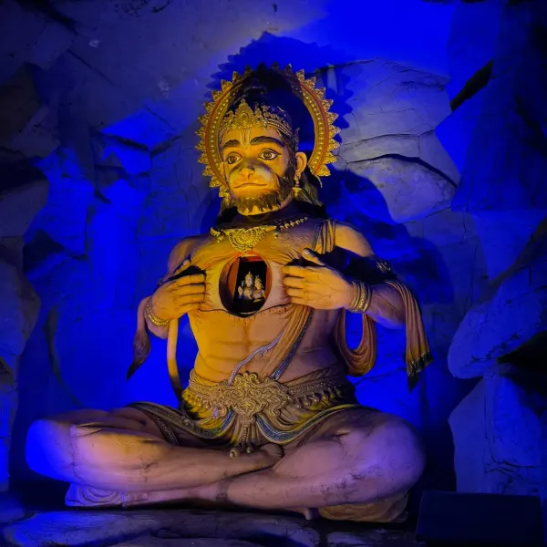 Statue of Hanuman opening his chest to reveal Rama and Sita, lit in blue inside a grotto