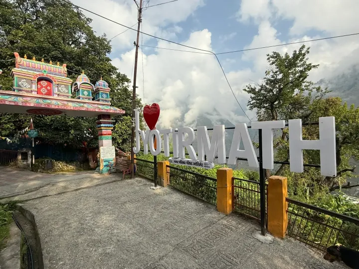 The Jyotirmath welcome sign in Joshimath with a colourful temple gate and cloud-covered mountains behind