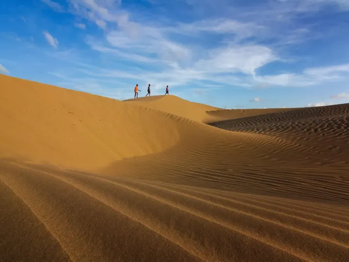Three figures walking along the crest of a sand dune in the Thar Desert