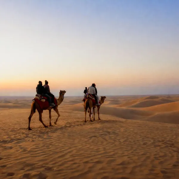 Camel riders crossing the dunes of the Thar Desert at sunset
